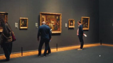Müzedeki sanat eserlerini bulanık arka planda gözlemleyen insanlar kapalı mekanlarda resim sergiliyorlar. Işıklar, sanatın değerini ve kültürel keşiflerin özünü yansıtıyor..