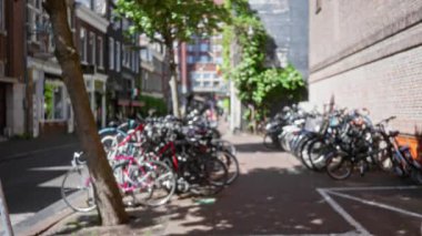 Amsterdam, Hollanda 'da bulanık bir caddeye park etmiş bisiklet, canlı şehir ortamında yürüyen insanlarla birlikte şehir yaşamını gözler önüne seriyor..