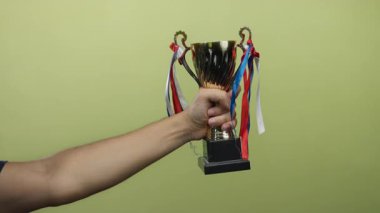 Sarı bir duvara altın kupa taşıyan beyaz bir adam, kutlama ve başarıyı gösteren kurdeleler..