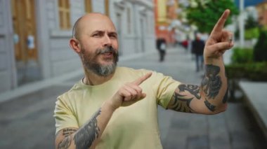 Şehirde gündüz vakti sakallı ve dövmeli bir adam açık havada kel kafasıyla mutlu bir yüz ifadesi sergiliyor..