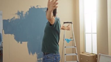 Orta yaşlı bir adam oturma odasını merdiven ve karton kutularla boyarken sevinçle yeni evini kucaklıyor..