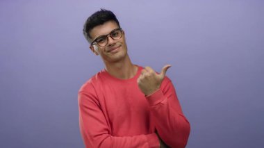 Gözlüklü ve kırmızı gömlekli genç adam mor arka planda duruyor. Ayrı bir ortamda başparmak hareketlerini güven ve cazibeyle gösteriyor.