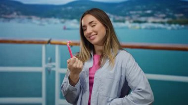 Tekne gezisindeki genç kadın elinde jiletle deniz kenarında manzaralı su manzarası sunuyor.