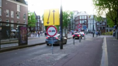 Arka planda trafik işaretleri, arabalar ve bulanık yayaların olduğu bulanık bir Avrupa caddesi manzarası şehir ortamında odak dışı rüya gibi bir etki yaratıyor.