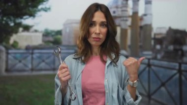 Antik Roma harabelerinin önünde İngiliz anahtarı tutan genç İspanyol kadın modern aletleri tarihi şehir dekoruyla harmanlıyor..