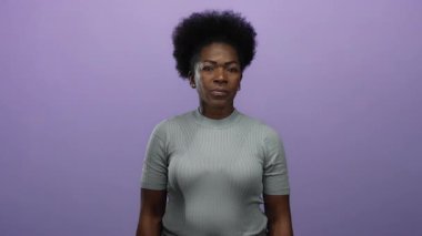 İzole edilmiş mor arka plana karşı onaylanmayan bir jest yapan Afro-Amerikan kadın, stüdyo ortamında net bir ifade ve vücut dili ile reddedildiğini gösteriyor.