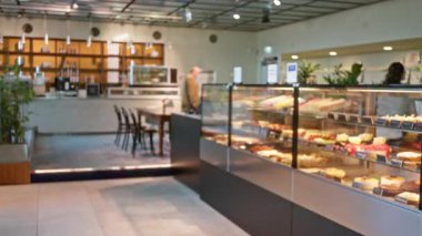 Modern bir kafede çeşitli tatlılar sergilenen bulanık hamur işleri sıcak ışıklandırma ve çözülmüş arka plan altında restoran ortamında tezgahın yanında görünen bir kadınla gösterilir.