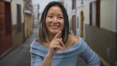 Şehirli bir sokak ortamında gülümseyen bir kadın, mutluluk, gizlilik, sessizlik ve gençlik kavramlarını canlandırıyor, canlı bir şehir sahnesinde yakalanmış..