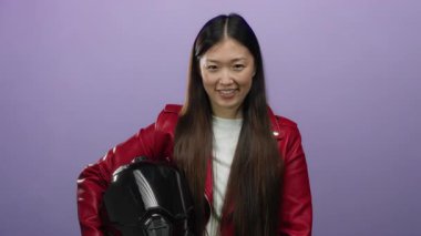 Stüdyoda kaskını tutarak gülümseyen bir kadın zarif kırmızı ceketiyle modern yaşam tarzını aktaran münferit mor arka plana karşı..