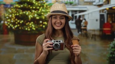 Elinde kamera ve dondurma külahıyla gülümseyen kadın ışıl ışıl ışık ve kentsel ortam ile güçlendirilmiş şenlik arka planına sahip..