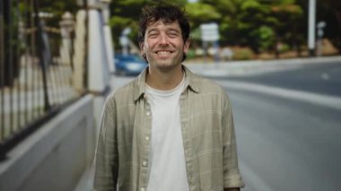 İspanyol bir adam sokakta sessiz bir jest yapıyor, açık havada günlük ekose gömlek giyiyor şehir manzarasının bulanık arka planı ve uzaklardan geçen arabalar var..