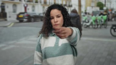 Arka planda insanlar ve bisikletlerle sokakta el kol hareketi yapan genç İspanyol kadın, canlı bir şehirde şehir manzarası yakalıyor..