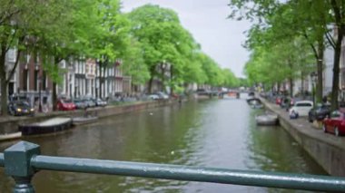 Mimarisi, ağaçları ve bulutlu gökyüzünün altında deniz boyunca park etmiş arabaları olan amfi kanalların görüntüsü.