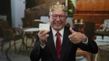 Takım elbiseli kıdemli bir adam ve kartvizit tutuyor ve restoran düzeninde baş parmağını kaldırıyor..