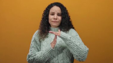 Süveter giyen kadın ellerini turuncu bir duvara dayayıp düşünceli bir hareket göstererek mola veriyor..