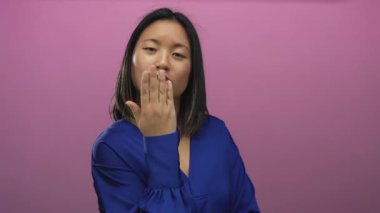 Gülümseyen ve mavi gömlekli bir kadın canlı pembe arka planda genç ve neşeli bir yüz ifadesi sergiliyor.