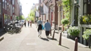 Güneşli bir Amsterdam caddesinde bisiklet ve yeşillikle yürüyen bulanık insanlar büyüleyici şehir manzarası.