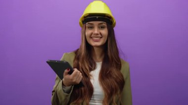 Sarı kask takan genç bir mimar, elinde tablet tutarak modern mesleki kariyerini gözler önüne seriyor.