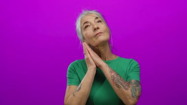 Yeşil tişörtlü yaşlı kadın izole edilmiş pembe duvar arkasına gülümsüyor, sakin ve barışçıl duygular taşıyor, kolunda dövmesi var..