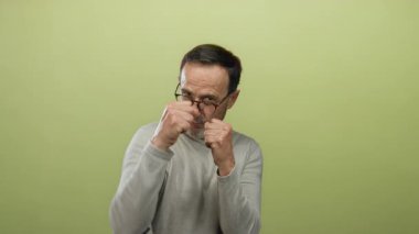 Sarı arka planda yumrukları havada poz veren adam kararlılık ve kendine güven gösteriyor..