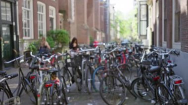 Arka planda yürüyen, canlı şehir yaşamını ve geleneksel Avrupa mimarisini gözler önüne seren bulanık insanların olduğu Amsterdam 'da bir caddeye park edilmiş bisikletler..