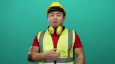Sarı kasklı ve çelik yelekli bir adam yeşil duvar arka planına karşı şükranlarını sunuyor.