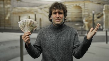Elinde Rus rublesi olan İspanyol bir adam şehir sokaklarında şaşkın görünüyor. Şehir merkezindeki para sorunlarını vurguluyor..