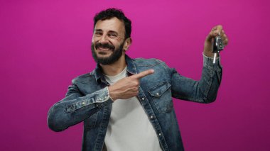 Sakallı bir adam arabanın anahtarlarını tutarken gülümsüyor.