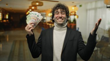 Bir otel resepsiyonunda elinde Arjantin pezosu tutarken gülümseyen İspanyol bir adam zenginlik ve neşe sergiliyor..