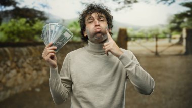 Bangladeş 'li İspanyol bir adam parkta komik bir yüz ifadesi sergiliyor, banknotları tutarken şakacı hareketler yapıyor, doğal bir ortamda ifade ve para karışımı sergiliyor..