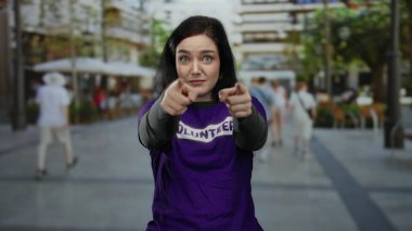 Bulanık insanların ve kentsel çevrenin geçmişine sahip hareketli caddede kameraya güvenle bakan gönüllü tişört giyen bir kadın..