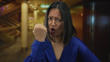 Mavi gömlekli Çinli kadın kapalı bir otel odasında yumruğunu sıktığını ve şehir ortamında güçlü duygular beslediğini ifade ediyor..