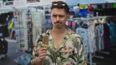 Genç İspanyol adam canlı bir açık hava pazarında dondurma yiyor. Etrafı giysi tezgahları ve şehir manzaralarıyla çevrili. Şehir turizmini yakalıyor..