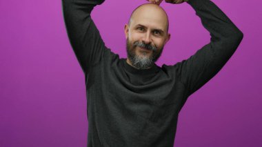 Sakallı kel bir adam gülümsüyor ve canlı pembe bir arkaplanda poz veriyor. Çekici ve neşeli bir izole görüntü yaratıyor..