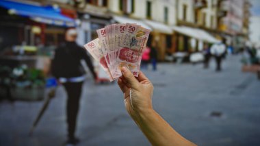 Kalabalık bir şehir ortamında yatırım potansiyeli ve finansal işlemleri tasvir eden bir şehir caddesinde Meksika banknotları tutan bir adam..