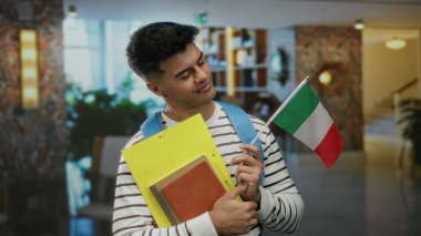 Otelin içinde coşkuyla İtalyan bayrağı tutan genç bir adam, seyahat ve kültürel bağlantıyı sembolize eden belgeler taşıyor..