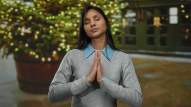 Gecenin bir yarısı şehir caddesinde, şenlikli ışıkların önünde huzur içinde meditasyon yapan bir kadın, sakin ve huzurlu bir ifade sergiliyor..