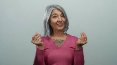 Gri saçlı yaşlı kadın, izole edilmiş beyaz bir arka plana karşı para hareketi yapıyor. Dövmeli pembe bir kazak giyiyor, ifade ve jest yapıyor..