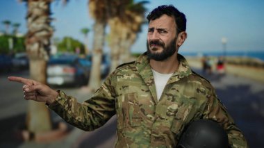 Askeri üniformalı İspanyol bir adam, güneşli bir caddede arka planda palmiye ağaçları olan ve yönünü ve amacını bildiren açık havayı işaret ediyor..