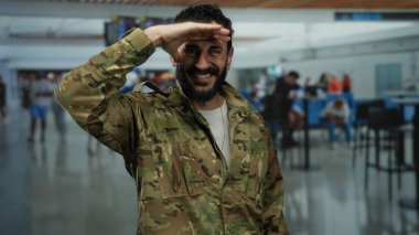 Askeri üniformalı İspanyol bir adam hareketli bir havaalanı terminalinde selamlıyor. 1 numaralı terminaldeki kalabalık arasında bir saygı anı yakalıyor..