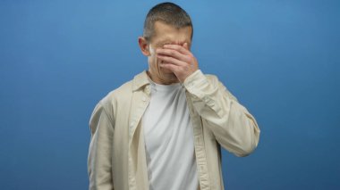 Üzüntüyle yüzünü kapatan adam mavi arka planda duygu ve yalnızlık gösteriyor..
