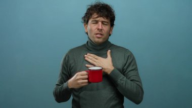 Kırmızı kahve fincanını mavi arka planda tutan yakışıklı görünümlü İspanyol bir adam rahatsızlığını ya da hastalığını ifade ediyor..