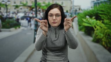 Yoğun bir caddede çapraz ellerle el kol hareketi yapan bir kadın, canlı bir şehir çevresiyle çevrili, ciddi bir ifadeyle reddedilmeyi reddediyor..