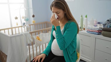 Bebek odasında bebek kıyafetleri ve aksesuarlarıyla çevrili bir beşikte ağlayan hamile bir kadın..