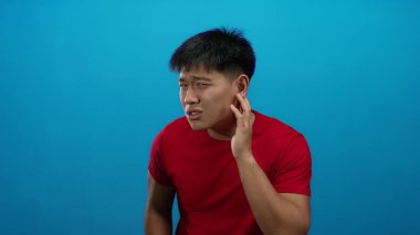 Kırmızı tişörtlü, mavi arka planda kafası karışmış genç bir adam.