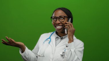 Cep telefonunda steteskopla konuşan ve gülümseyen bir kadın, yeşil bir duvarın karşısında izole edilmiş, iletişimde bir tıp uzmanını öneriyor, dostça bir nişanı vurguluyor..