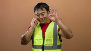 Sarı yelek giyen bir adam akıllı telefonda konuşurken gülüyor ve kahverengi arka planda iyi bir hareket gösteriyor..