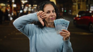 Bir kadın elinde Yuan banknotları tutarken, gece bir şehir caddesinde onaylamadığını belirterek, Çin para birimiyle mali hoşnutsuzluğu ve kentsel ambiyansı vurguluyor..