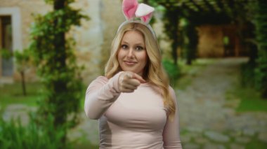 Akdeniz taşından bir evde neşeli bir şekilde el kol hareketi yapan tavşan kulaklı bir kadın, yemyeşil, neşeli ve neşeli bir atmosfer taşıyor..