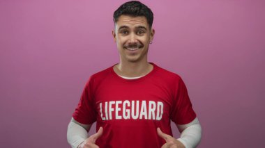 Kırmızı tişörtlü genç İspanyol cankurtaran canlı pembe bir arka plana karşı güvenle gülümsüyor, modern bağlamda güvenliği ve tarzı temsil ediyor..